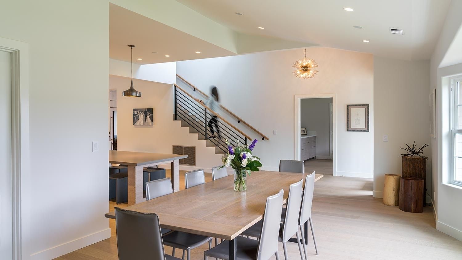 Bright and open dining area with a large table, modern chandelier, and a staircase leading to the upper floor.